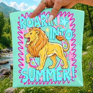 May include: A light teal tote bag with the words "ROARIN' INTO SUMMER!" in turquoise, outlined in pink. A cartoon lion with a yellow body and orange mane is featured. Stars and wavy lines complete the design.