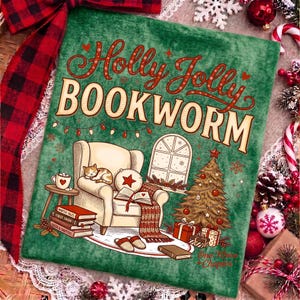 Op de afbeelding: Een groene pluche deken met de tekst Holly Jolly BOOKWORM, een comfortabele fauteuil met een slapende kat, een stapel boeken, een kerstboom en een raam. Het ontwerp bevat rode en witte accenten, een lichtsnoer en kerstcadeaus.