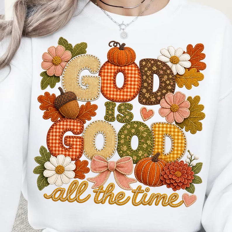 Pu&ograve; includere: Una felpa bianca con un design grafico che riporta il testo "GOD IS GOOD all the time". Le lettere sono riempite con vari motivi autunnali tra cui quadri, fiori e texture, circondate da zucche, foglie e fiori.