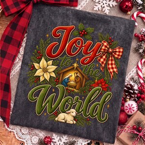 Może przedstawiać: Ciemnoszara tkanina z kolorową grafiką i napisem Joy to the World. Wz&oacute;r przedstawia scenę narodzin z postaciami, białą gwiazdę betlejemską, czerwone jagody, zielone gałązki sosny oraz czerwono-białą kokardę w kratę jako akcent.
