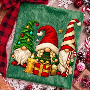 Puede incluir: Un cuadrado de tela verde con tres gnomos. El gnomo de la izquierda lleva un gorro de &aacute;rbol de Navidad con adornos. El gnomo central tiene trenzas rubias, un gorro rojo y sostiene un regalo rojo. El gnomo de la derecha lleva un gorro a rayas.