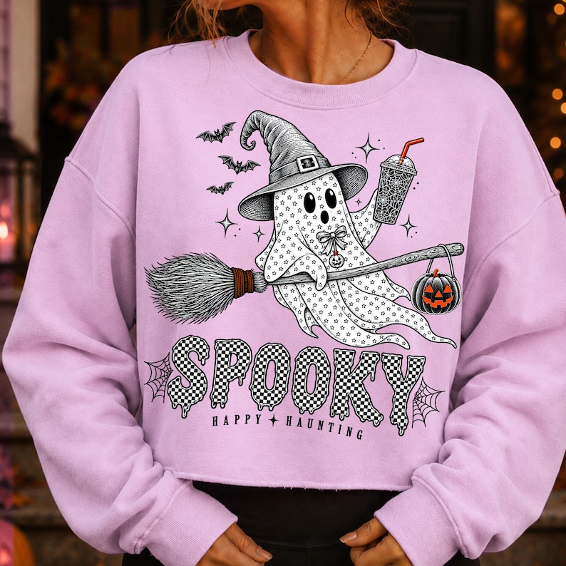 May include: A light purple long-sleeve sweatshirt featuring a graphic of a ghost wearing a witch hat, riding a broomstick, and holding a drink. The design includes bats, a jack-o'-lantern, and the text SPOOKY HAPPY HAUNTING in a checkered pattern.