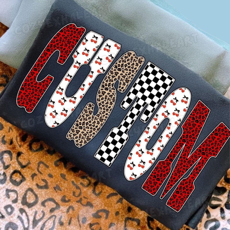 May include: A dark gray pillow with the word "CUSTOM" in large, stylized letters. The letters feature various patterns, including red leopard print, white with cherries, brown leopard print, and black and white checkered patterns.