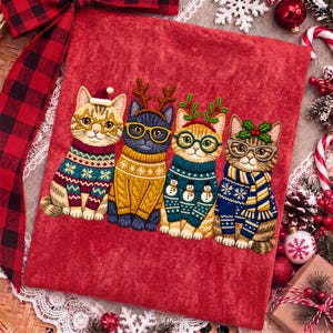 May include: A red fabric panel featuring an embroidered illustration of four cats wearing colorful winter sweaters and glasses. The cats are adorned with festive accessories including a Santa hat, reindeer antlers, holly leaves, and a scarf.