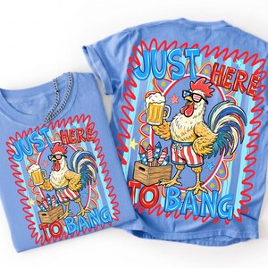 May include: Two light blue t-shirts with a rooster graphic. The rooster wears sunglasses and striped shorts, holding a beer and standing near a crate of fireworks. Text reads "JUST HERE TO BANG" in red and blue.