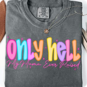 May include: A gray Comfort Colors t-shirt with the phrase "only hell My Mama Ever Raised" in colorful bubble letters. A silver necklace with a small pendant rests on the shirt. The shirt is a size small.
