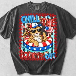 Op de afbeelding: Donkergrijze t-shirt met een luipaard met een zonnebril en een patriottische hoed, drijvend in een rood, wit en blauw zwemband. Het shirt heeft de tekst "CHILL THE FOURTH OUT" in een speels lettertype, ter viering van Independence Day.