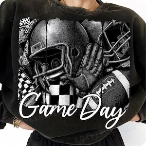 May include: Black and white graphic sweatshirt featuring football helmets, a glove, and a football. The words "Game Day" are written in a white script across the bottom of the design. The design includes a checkered flag.