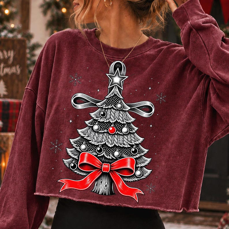 K&ouml;nnte beinhalten: Ein bordeauxrotes, lang&auml;rmeliges bauchfreies Sweatshirt mit einer Grafik eines stilisierten Weihnachtsbaums. Der Baum ist mit einer gro&szlig;en roten Schleife an der Basis, einem Stern an der Spitze und kleinen Kugeln verziert, umgeben von wei&szlig;en Schneeflocken.