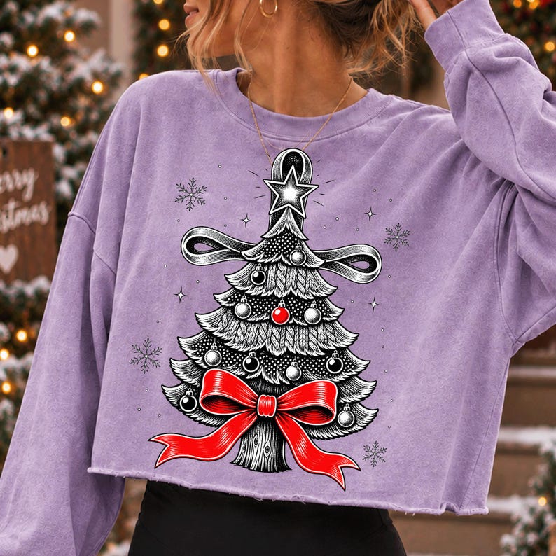 K&ouml;nnte beinhalten: Ein hellviolettes, lang&auml;rmeliges bauchfreies Sweatshirt mit einer Grafik eines stilisierten Weihnachtsbaums. Der Baum ist mit einer gro&szlig;en roten Schleife an der Basis, einem Stern an der Spitze und kleinen silbernen und roten Kugeln verziert, umgeben von Schneeflocken.