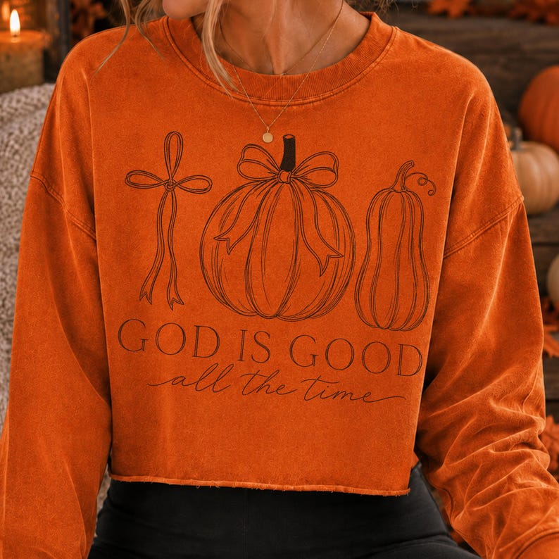 K&ouml;nnte beinhalten: Ein lang&auml;rmeliges Sweatshirt in gebranntem Orange mit einem Saum mit Rohkante. Die Vorderseite zeigt eine schwarze Strichzeichnung eines Kreuzes mit Schleife, eines K&uuml;rbisses mit Schleife und eines K&uuml;rbisgew&auml;chses. Der Text lautet "GOD IS GOOD all the time".