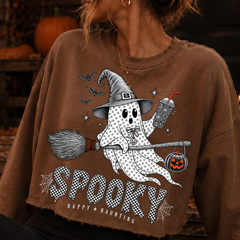 May include: A brown cropped sweatshirt featuring a graphic of a ghost wearing a witch hat, riding a broomstick, and holding a drink. The ghost is decorated with stars and a bow. Below, the text reads SPOOKY and HAPPY HAUNTING in a checkered pattern.
