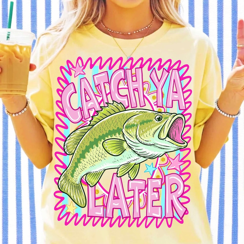 Op de afbeelding: Geel T-shirt met een afbeelding van een groen en gele vis met open mond. De tekst "CATCH YA LATER" is roze, omlijnd met een golvend blauw en roze ontwerp. Het shirt heeft een casual stijl.