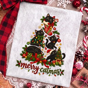 K&ouml;nnte beinhalten: Ein hellgrauer Stoff mit einer Grafik von f&uuml;nf schwarzen Katzen in Tannenbaumform, verziert mit Weihnachtskugeln, Lichterketten und einem Strumpf. Der Schriftzug "merry catmas" ist unten in roter und gr&uuml;ner Schrift mit kleinen Lichtern.