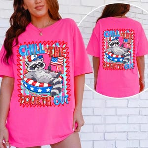 Op de afbeelding: Een felroze t-shirt met een cartoon wasbeer met een zonnebril en een patriottische hoed, liggend in een rood, wit en blauw zwemband. De tekst "CHILL THE FOURTH OUT" staat boven en onder de wasbeer.