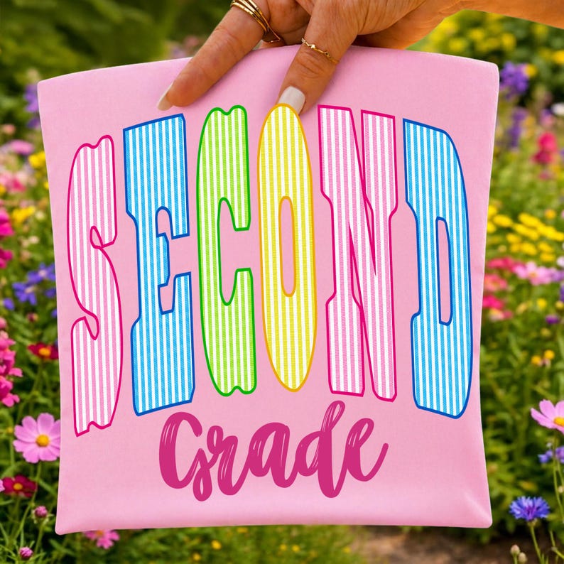 May include: A light pink fabric pouch featuring the text SECOND in large, vertical, multi-colored striped letters including pink, blue, green, and yellow. Below the word SECOND, the word Grade is printed in a dark pink cursive script font.