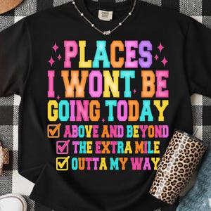 K&ouml;nnte beinhalten: Schwarzes T-Shirt mit dem Text "PLACES I WON'T BE GOING TODAY" in leuchtenden Farben. Das Shirt zeigt auch die S&auml;tze "ABOVE AND BEYOND", "THE EXTRA MILE" und "OUTTA MY WAY". Ein Becher mit Leopardenmuster ist sichtbar.