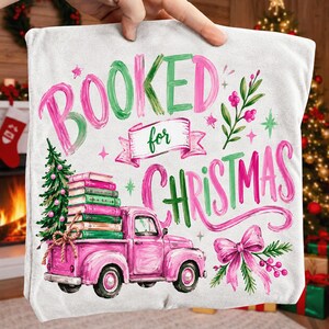 May include: A white throw pillow featuring a pink vintage truck carrying a stack of books and a small Christmas tree. The text reads "BOOKED for CHRISTMAS" in pink and green brush-style lettering, accented with a pink bow and festive greenery.