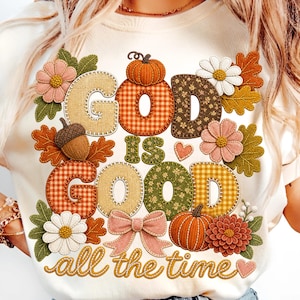 Pu&ograve; includere: Una t-shirt color crema con una grafica che riporta il testo "God is good all the time". Il design include elementi a tema autunnale come zucche, ghiande, fiori e foglie nelle tonalit&agrave; dell'arancione, marrone, verde e rosa con motivi a quadri.