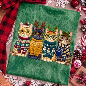 May include: A green fabric panel featuring an embroidered illustration of four cats wearing holiday sweaters and glasses. The first cat wears a Santa hat, the second has reindeer antlers, the third has holly, and the fourth has a scarf.