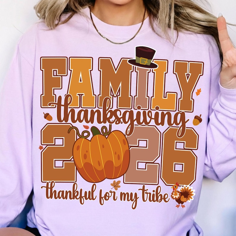 Pode incluir: Uma camisola de manga comprida em roxo claro com um gr&aacute;fico que inclui o texto "FAMILY thanksgiving 2026" e "thankful for my tribe". O design apresenta uma ab&oacute;bora castanha, um chap&eacute;u de peregrino, bolotas, folhas e um peru.