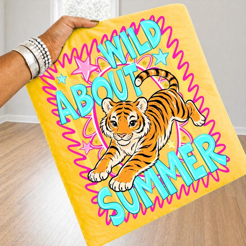 K&ouml;nnte beinhalten: Gelbe Decke mit einer Cartoon-Tiger-Illustration. Auf der Decke stehen die Worte "WILD ABOUT SUMMER" in T&uuml;rkis und Pink. Der Tiger ist orange und schwarz.