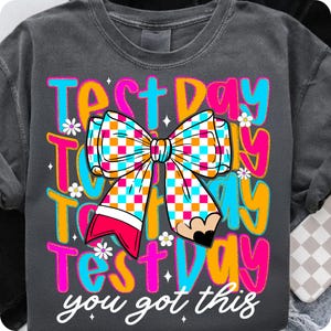 Puede incluir: Una camiseta gris oscuro con el texto "Test Day Test Day Test Day you got this" en rosa, naranja, azul y amarillo. Un lazo a cuadros rosa, naranja y blanco está en el centro del texto.
