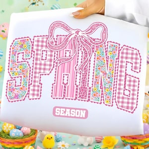 Könnte beinhalten: Weißes Kissen mit dem Wort "SPRING" in Rosa, mit einer Schleife und floralen und gemusterten Designs. Das Wort "SEASON" steht unter dem Wort "SPRING".