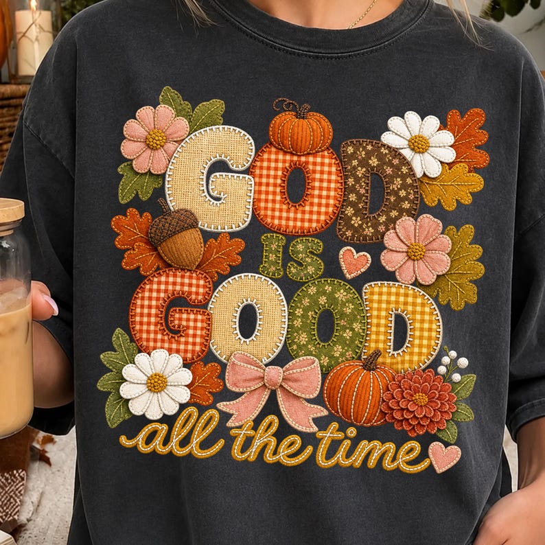 Pu&ograve; includere: Una t-shirt grigio antracite con una grafica che riporta il testo "GOD IS GOOD all the time" in uno stile a tessuto cucito. Il design include zucche, foglie autunnali, margherite, una ghianda e un fiocco rosa nei colori dell'autunno.