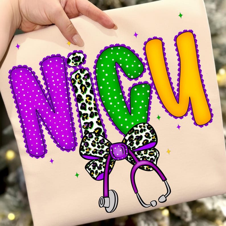 May include: A light beige shirt with the word "NICU" in large, colorful letters. The letters are purple, green, and yellow, with a leopard print bow and a purple stethoscope. The design includes white polka dots and decorative purple trim.