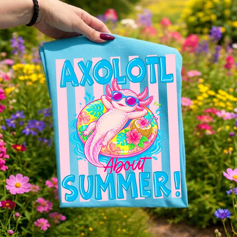 Peut inclure: Une serviette bleu clair avec les mots "AXOLOTL About SUMMER!" dans une police ludique. Le motif repr&eacute;sente un axolotl de dessin anim&eacute; portant des lunettes de soleil et flottant sur une bou&eacute;e. Des rayures roses et bleues sont en arri&egrave;re-plan.
