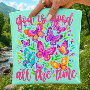 Peut inclure: Un sac fourre-tout turquoise clair avec l'inscription "Goa is good all the time" en rose. Le sac est orn&eacute; de papillons color&eacute;s dans les tons de rose, orange, violet et turquoise, entour&eacute;s de feuilles et d'&eacute;toiles vertes.