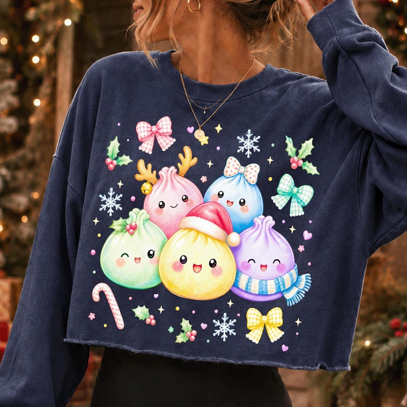 May include: A navy blue long-sleeve cropped sweatshirt featuring a graphic print of five colourful, smiling dumpling characters. The dumplings are decorated with a Santa hat, a blue scarf, and reindeer antlers, surrounded by bows, snowflakes, and holly.