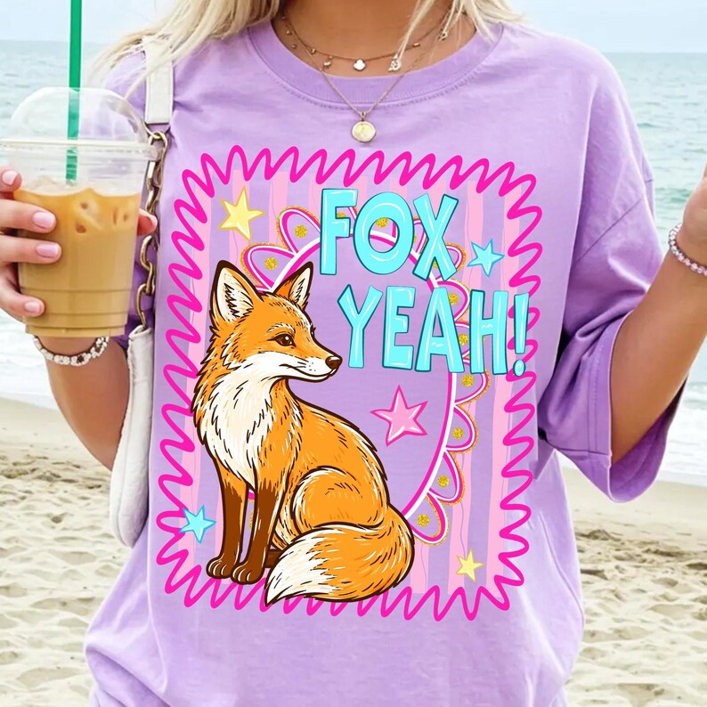 Op de afbeelding: Een lichtpaars T-shirt met een cartoonvos en de tekst "FOX YEAH!". De vos is oranje en wit, in een roze en paars golvend kader met sterren. Het T-shirt heeft korte mouwen.