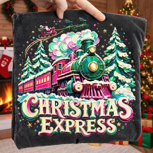May include: A dark grey t-shirt featuring a colourful graphic of a green and pink steam locomotive train, snow-covered pine trees, and a flying Santa sleigh. The text CHRISTMAS EXPRESS is printed in large, cream-coloured, stylised lettering below.