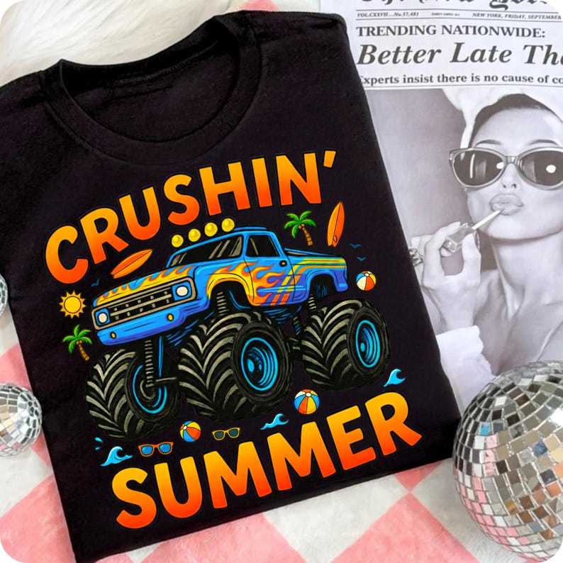 May include: Black t-shirt with a colorful graphic featuring a blue monster truck with flames, surfboards, and palm trees. The text "CRUSHIN' SUMMER" is in orange and yellow. The shirt has a crew neck.