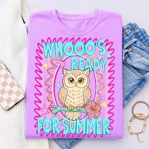 Peut inclure: T-shirt lilas avec un motif de hibou perch&eacute; sur une branche avec une fleur d'hibiscus. Le texte "WHOOO'S READY FOR SUMMER" est en turquoise, avec une bordure rose et jaune. Le t-shirt est pli&eacute;, avec un pull blanc, un jean et des accessoires en arri&egrave;re-plan.