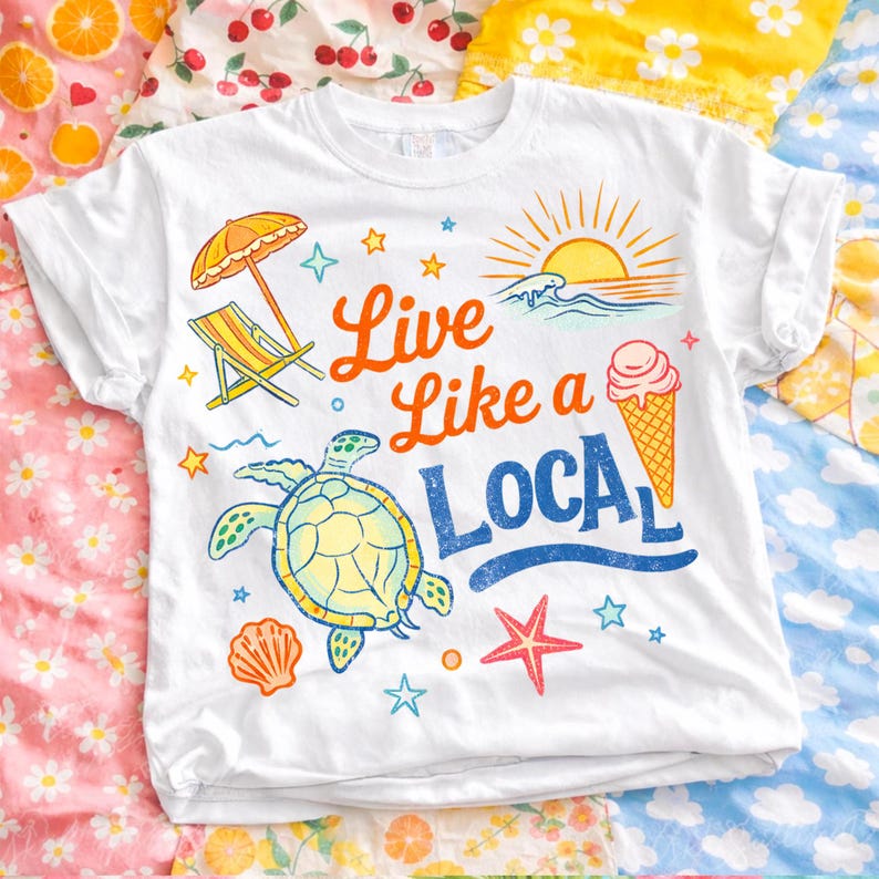 K&ouml;nnte beinhalten: Wei&szlig;es T-Shirt mit umgekrempelten &Auml;rmeln und einem farbenfrohen Strandmotiv. Das Design zeigt eine Schildkr&ouml;te, ein Eis, einen Strandstuhl und den Text "Live Like a Local". Das Shirt ist mit Sternen, einer Muschel und einem Seestern verziert.