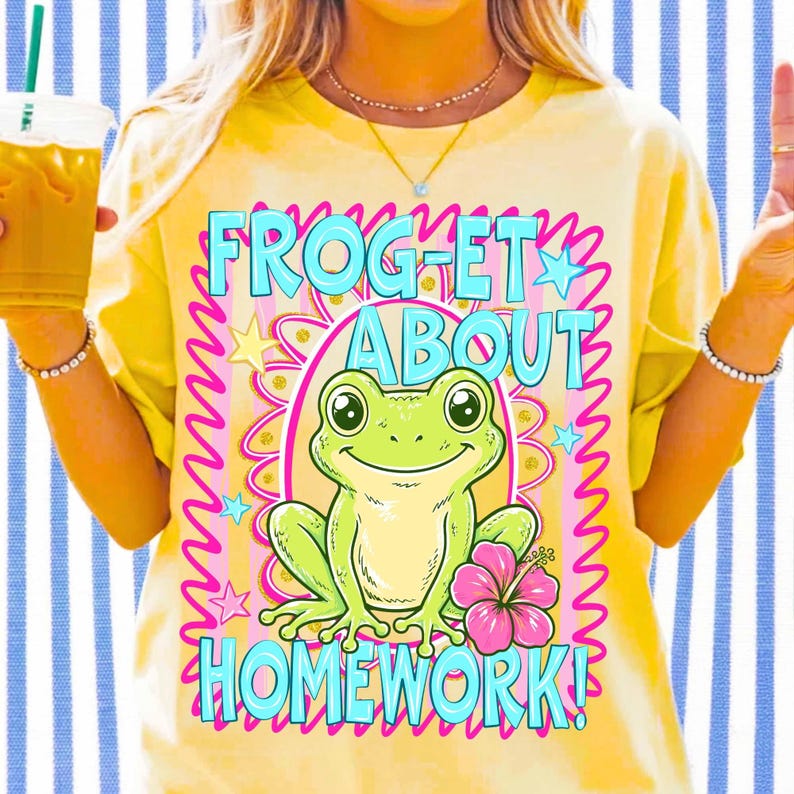K&ouml;nnte beinhalten: Gelbes T-Shirt mit einem Frosch-Cartoon und dem Text "FROGET ABOUT HOMEWORK!". Der Frosch ist gr&uuml;n mit einer rosa Blume. Der Text ist blau und rosa. Eine Person tr&auml;gt das T-Shirt und h&auml;lt ein Getr&auml;nk.