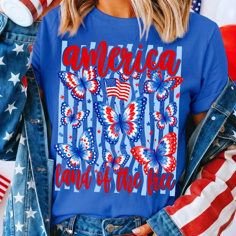 May include: A blue t-shirt featuring a graphic print of red, white, and blue butterflies, a small American flag, and the red text "america" at the top and "land of the free" at the bottom, layered over a light blue vertical striped background.
