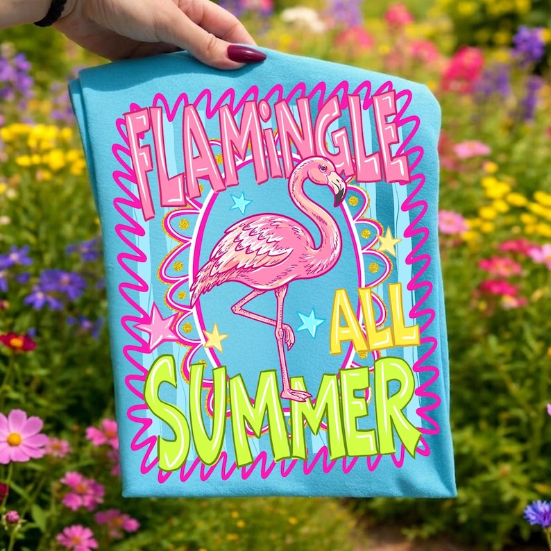 Puede incluir: Una camiseta azul claro con una ilustraci&oacute;n de un flamenco rosa y las palabras "Flamingle All Summer" en un dise&ntilde;o colorido. El flamenco est&aacute; de pie sobre una pata, rodeado de estrellas y un borde ondulado.