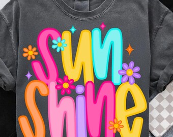 May include: A dark gray t-shirt with the words "sunshine" in colorful, stylized lettering. The letters are outlined in black and have a retro, groovy vibe. The shirt is decorated with small, colorful flowers.