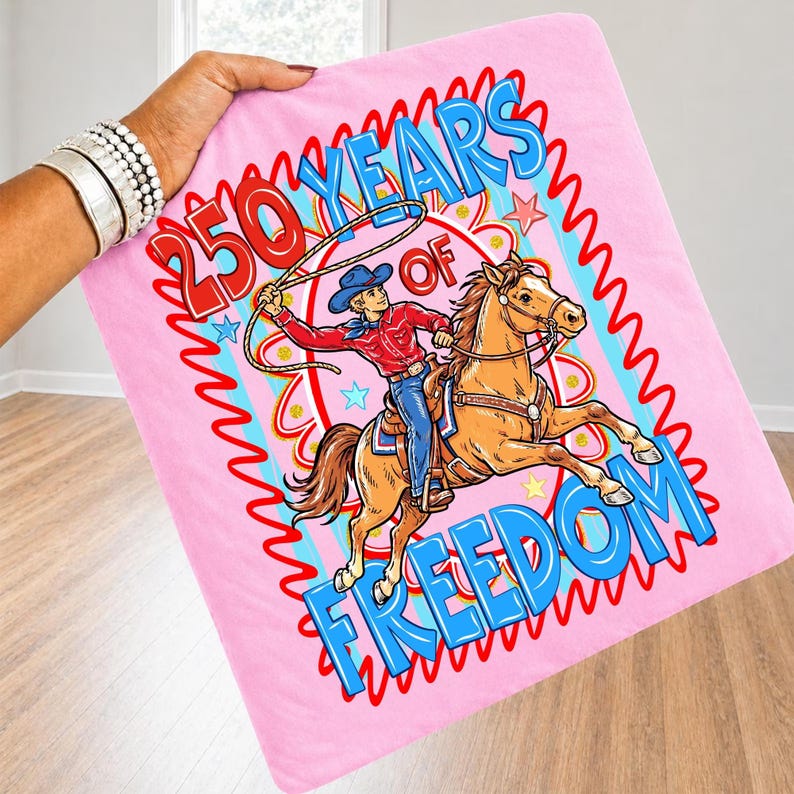 Puede incluir: Manta rosa con un vaquero a caballo con un lazo. El texto dice "250 YEARS OF FREEDOM" en rojo y azul. El vaquero lleva una camisa roja, vaqueros azules y un sombrero azul. La manta est&aacute; sujeta.