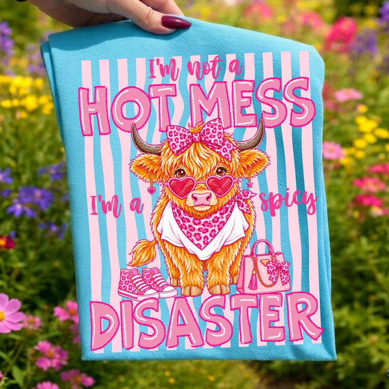 K&ouml;nnte beinhalten: Hellblaues Handtuch mit einer Cartoon-Illustration einer Highland-Kuh mit herzf&ouml;rmiger Sonnenbrille, Schleife und Halstuch. Der Text lautet: &bdquo;Ich bin kein hei&szlig;es Chaos, ich bin ein scharfes Desaster&ldquo;.