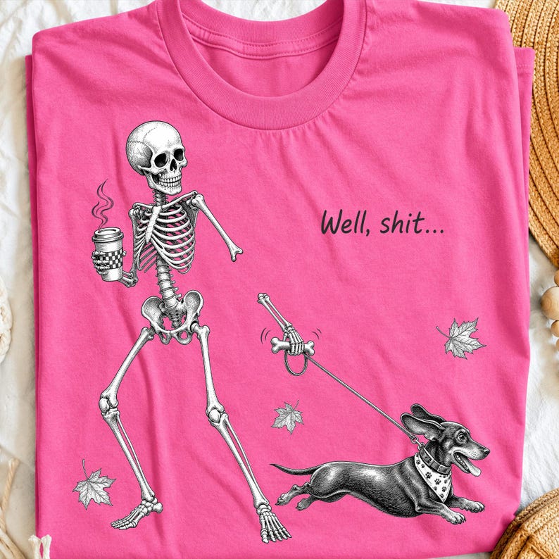 May include: A bright pink t-shirt featuring a black and white graphic of a skeleton holding a coffee cup and walking a dachshund on a leash. The skeleton holds a bone-shaped leash handle. The text "Well, shit..." is printed above the dog.
