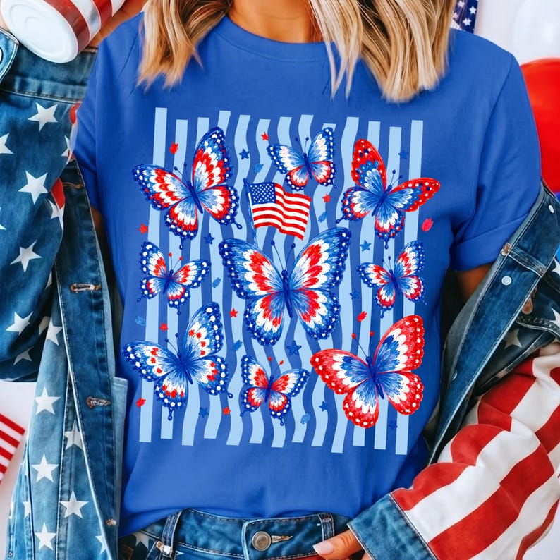 Puede incluir: Una camiseta azul real con un estampado gr&aacute;fico de varias mariposas con patrones de alas en rojo, blanco y azul. El dise&ntilde;o incluye una peque&ntilde;a bandera estadounidense y rayas verticales de color azul claro de fondo, acentuadas por peque&ntilde;as estrellas rojas.