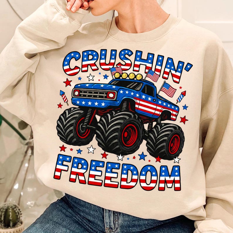 K&ouml;nnte beinhalten: Beiges Sweatshirt mit einem patriotischen Monster-Truck-Design. Der Truck ist blau mit roten und wei&szlig;en Akzenten, amerikanischen Flaggen und den Worten "CRUSHIN' FREEDOM" in Rot, Wei&szlig; und Blau.