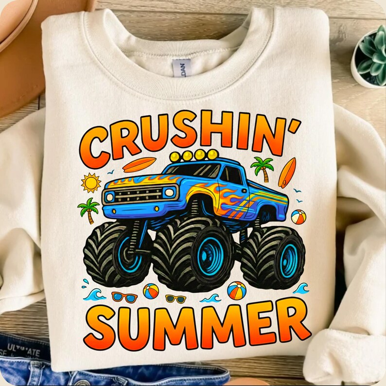 May include: Cream-colored sweatshirt with a colorful graphic of a blue monster truck with flames, palm trees, and the words "CRUSHIN' SUMMER" in orange and yellow. Includes images of a sun, surfboards, and beach balls.