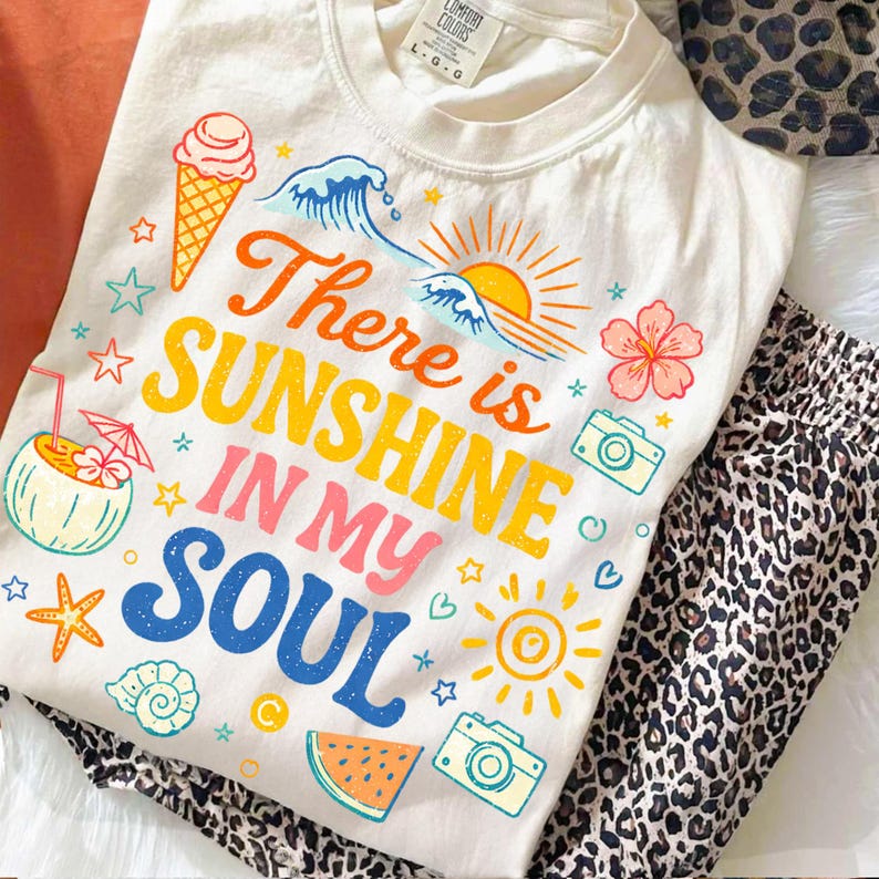 K&ouml;nnte beinhalten: Cremefarbenes T-Shirt mit dem Text "There is Sunshine in My Soul" in bunten Buchstaben. Das Shirt zeigt Illustrationen von Sonne, Eiswaffel, Wellen und anderen sommerlichen Grafiken. Kombiniert mit einer Hose mit Leopardenmuster.