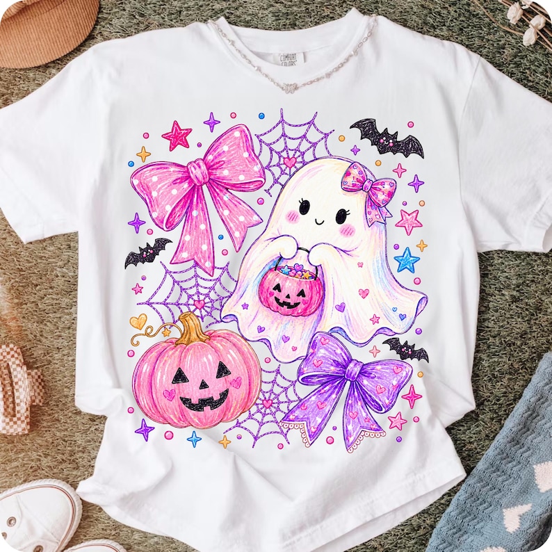 Peut inclure: Un t-shirt blanc avec une impression graphique color&eacute;e repr&eacute;sentant un fant&ocirc;me mignon tenant un seau citrouille, entour&eacute; de n&oelig;uds roses et violets, de toiles d'araign&eacute;e, de petites chauves-souris et d'&eacute;toiles. Le design utilise des tons vifs.